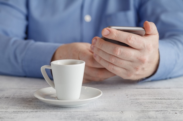 Mann sitzt mit Smartphone am Tisch mit Tasse Kaffee