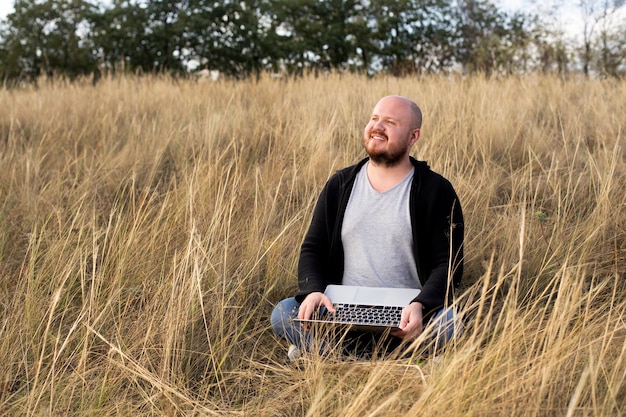 Mann sitzt und lächelt auf dem gras mit einem laptop