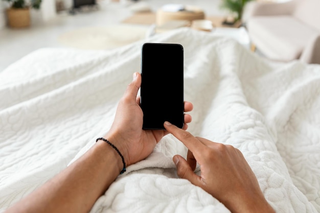 Mann SMS auf Smartphone mit leerem Bildschirm im Schlafzimmer POV