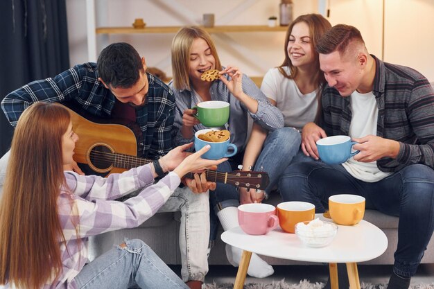 Mann spielt Akustikgitarre Gruppe von Freunden feiern zusammen drinnen