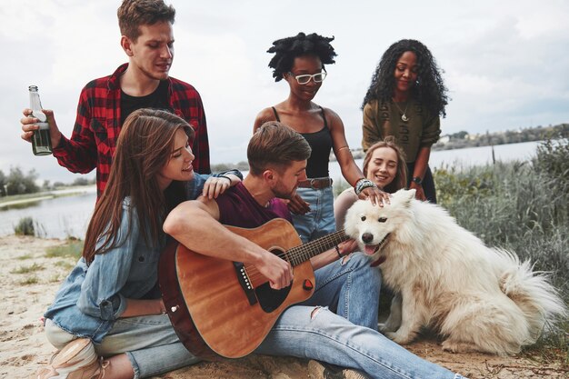 Mann spielt Gitarre. Eine Gruppe von Menschen hat ein Picknick am Strand. Freunde haben Spaß am Wochenende.