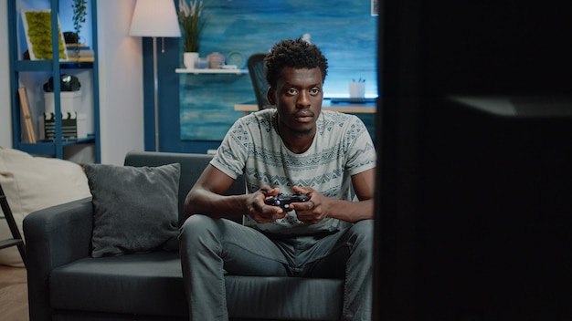 Mann spielt Videospiele auf der TV-Konsole mit Controller zur Unterhaltung. Junge Person, die Joystick für Online-Spiele im Fernsehen zu Hause hält. Spiele für Erwachsene und Spaß mit Gadgets.