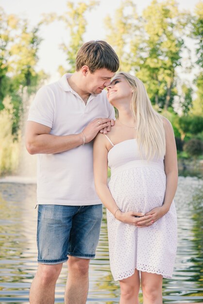 Mann spricht abends mit einer glücklichen schwangeren Frau am Kai in der Nähe des Wassers. Neue Familie erwartet ein Baby.