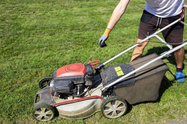 Mann startet den motor eines benzinrasenmähers, der auf dem gras steht