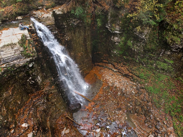 Mann steht auf der Klippe und blickt auf die Herbstzeit des Wasserfalls