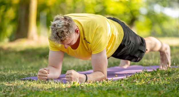 Mann steht in Plank-Position und praktiziert im Sommer Yoga im Freien. Mann macht Pilates-Training zur Dehnung der Muskeln und der Bauchmuskulatur