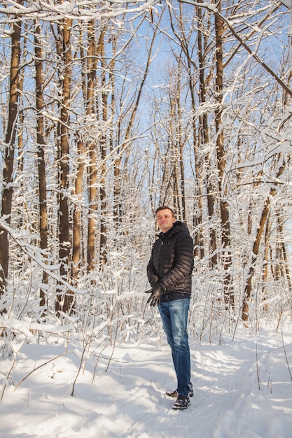 Mann stellt seinen Handschuh im Winterkiefernwald mit Schnee auf Bäumen und Boden an sonnigem Tag ein.