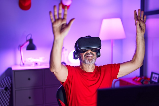 Mann Streamer mittleren Alters spielt Videospiel mit Virtual-Reality-Brille im Spielzimmer