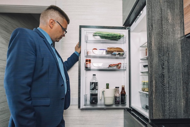 Mann sucht spät in der Nacht in einem offenen Kühlschrank in dunkler Küche nach Essen Der Mann sieht aus wie ein hungriger Junggeselle