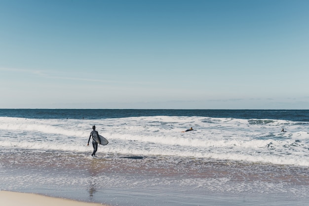 Mann-Surfer am Strand mit Surfbrett, Spaziergänge entlang der Küste Ozean