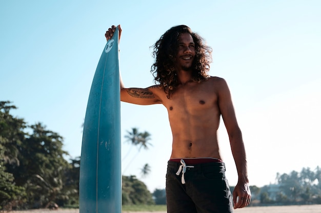 Mann-Surfer, der am Surfbrett am Sandstrand sitzt