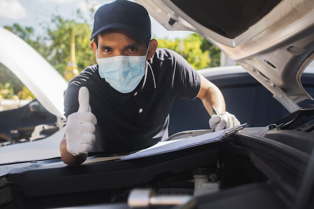 Mann trägt Gesichtsmaske, schützt Covid19 und überprüft den Autoservice in der Garage