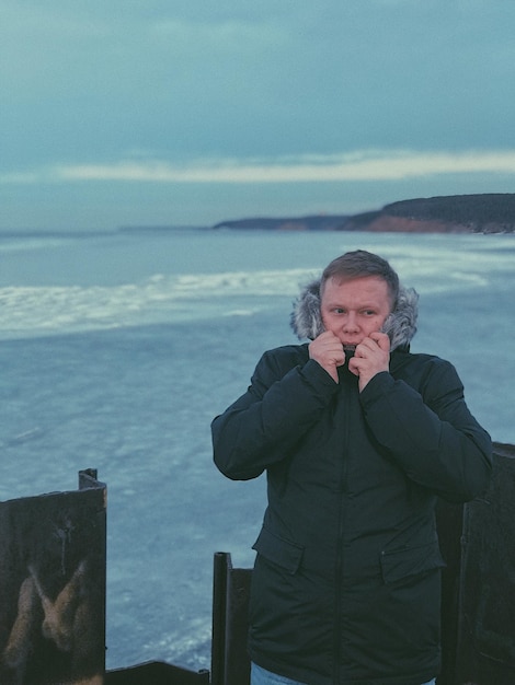 Foto mann trägt warme kleidung, während er gegen das meer steht