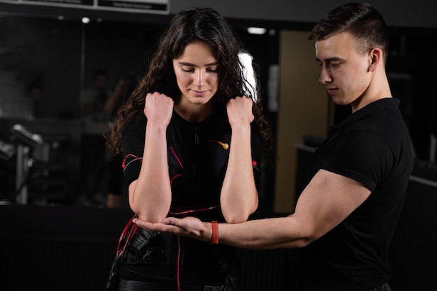 Mann Trainer trainiert ein Mädchen in einem EMS-Anzug im Fitnessstudio