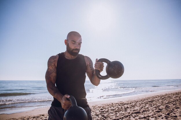 Foto mann trainiert mit kettlebells am strand gegen den himmel