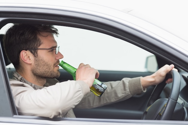 Mann trinkt Bier beim Autofahren