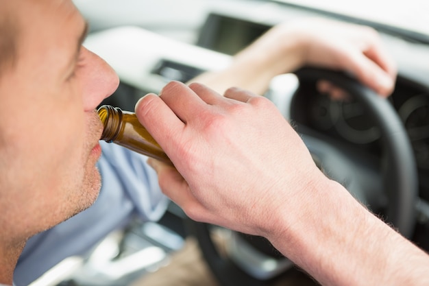 Mann trinkt Bier beim Autofahren