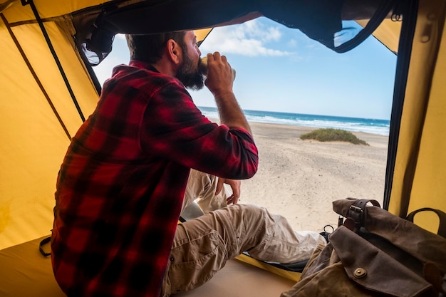 Foto mann trinkt saft, während er im zelt am strand gegen den himmel sitzt