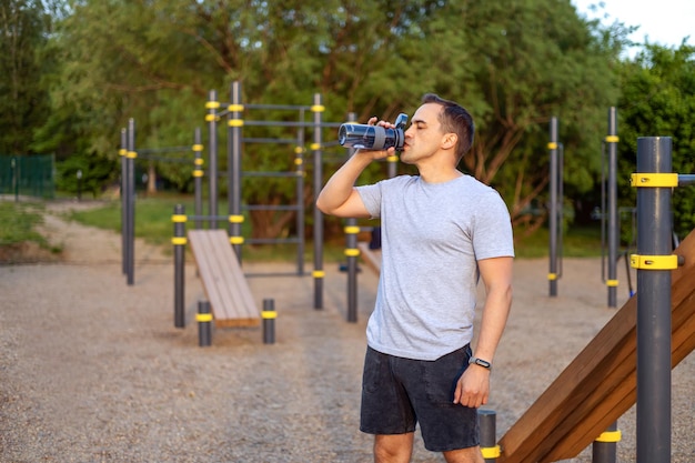 Mann trinkt Wasser aus einer Sportflasche auf einem öffentlichen Sportplatz