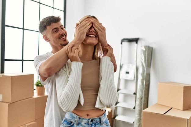 Mann überrascht seine Freundin, die im neuen Zuhause die Augen mit den Händen bedeckt