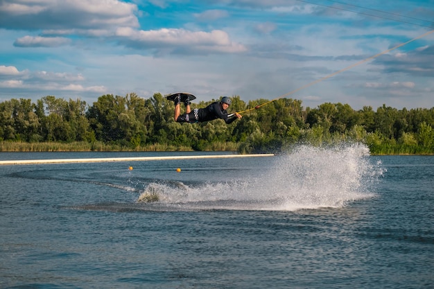 Mann übt Tricks auf dem Wakeboard, springt über Wasser und hält sich am Abschleppseil fest