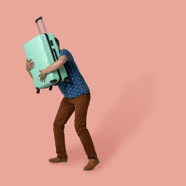 Mann umarmt einen Koffer, der ihn beim Posieren vor sich hält