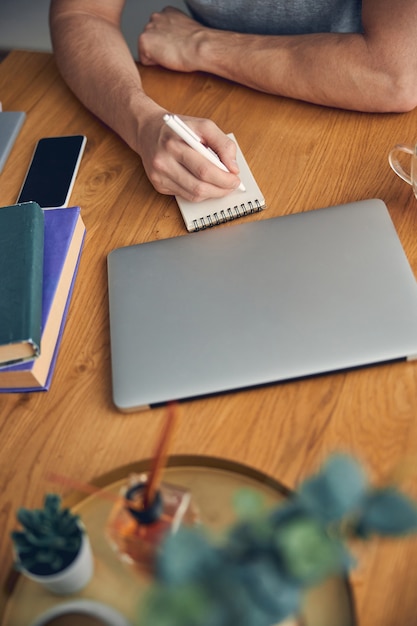 Mann, umgeben von Laptop und Büchern auf dem Tisch, der wichtige Informationen notiert