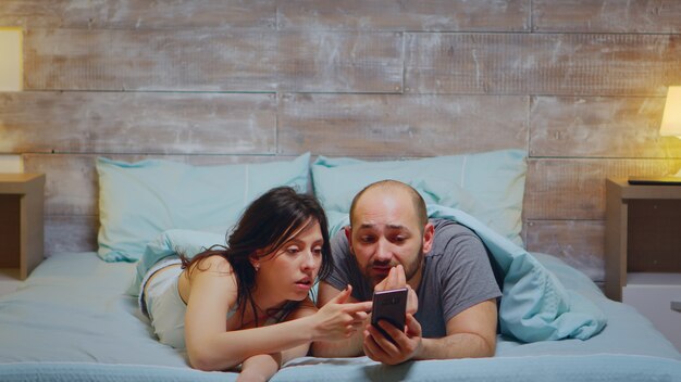 Mann und Frau benutzen das Telefon, während sie im Schlafanzug im Bett liegen.