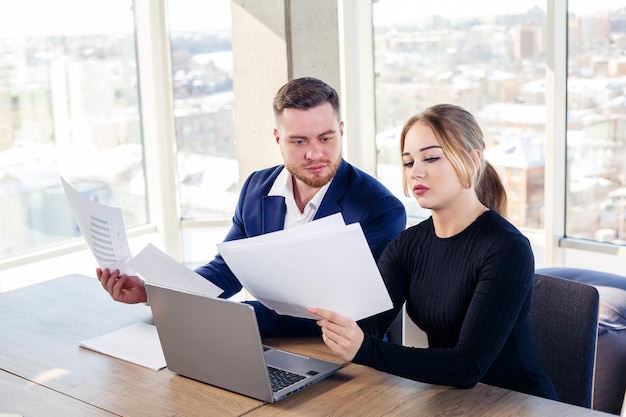 Mann und Frau Büroangestellte des Managers an ihrem Arbeitsplatz hinter einem Laptop und Dokumenten