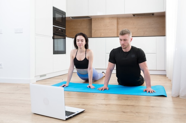 Mann und Frau des jungen Paares, die Fitness zu Hause online unter Verwendung des Laptops tun, online mit Trainer auf Boden zu Hause Sport treibend