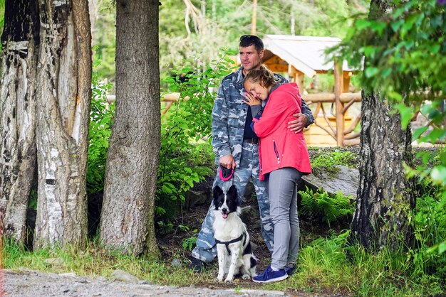 Mann und Frau, die einen Hund in der Natur umarmend stehen.