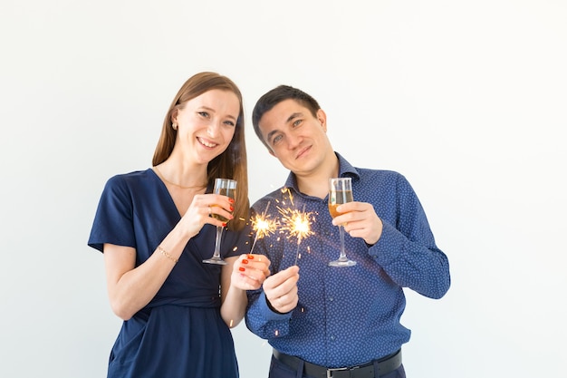 Mann und Frau, die Weihnachts- oder Silvesterparty mit bengalischen Lichtern und Gläsern Champagner auf weißem Hintergrund feiern.