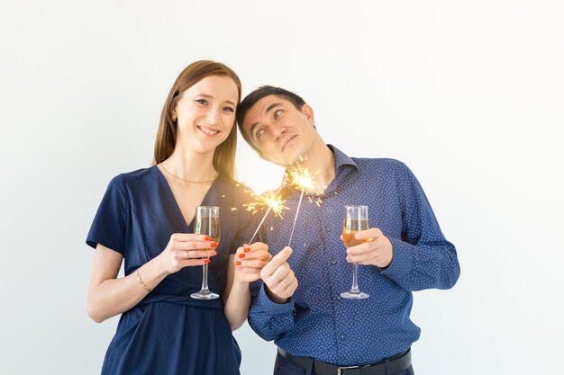 Mann und Frau, die Weihnachts- oder Silvesterparty mit bengalischen Lichtern und Gläsern Champagner auf weißem Hintergrund feiern.