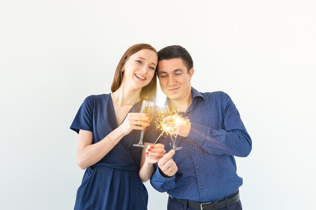 Mann und Frau, die Weihnachts- oder Silvesterparty mit bengalischen Lichtern und Gläsern Champagner auf weißem Hintergrund feiern.