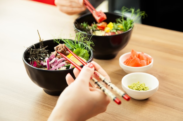 Mann und Frau essen Poke-Salat mit Stäbchen tupfen Thunfischsalat in eine Schüssel Leute im Restaurant