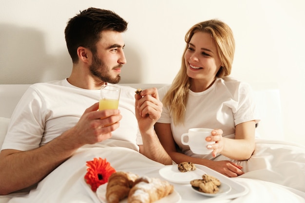 Mann und Frau haben köstliches französisches Frühstück, das im Bett liegt