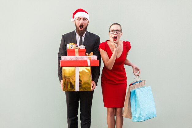 Mann und Frau im roten Kleid, die Weihnachtsgeschenke und -pakete halten und mit Wundergesicht schauen