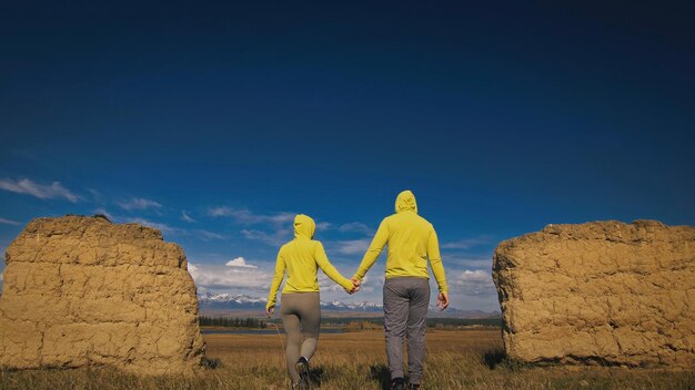 Mann und Frau in gelbgrüner Sportbekleidung Schönes Paar Reisende umarmt und küsst sich in der Nähe von altem Stein und genießt die Hochlandlandschaft