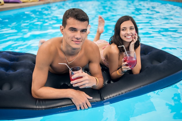 Mann und frau liegen auf einer matratze im pool mit cocktails