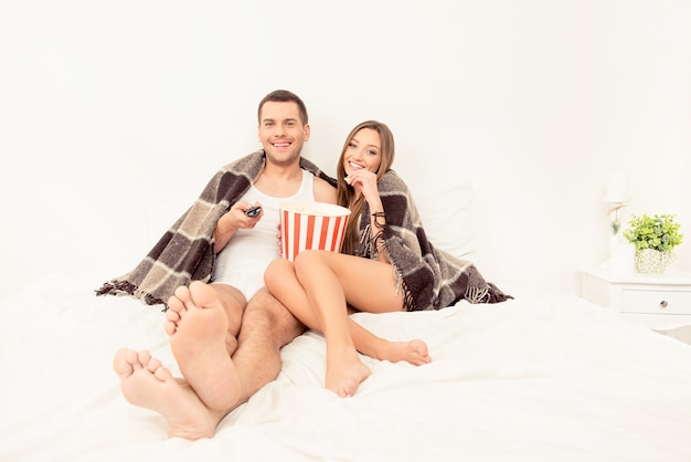 Mann und Frau liegen im Bett und schauen Film mit Popcorn