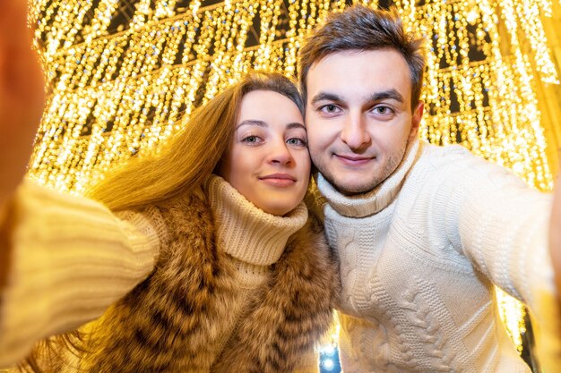 mann und frau machen nachts ein selfie vor dem hintergrund brennender lichter einer girlande im freien