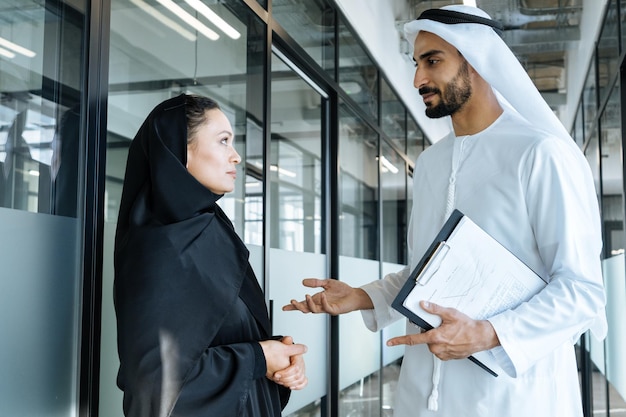 Mann und Frau mit traditioneller Kleidung der Emirate, die in einem Geschäftsbüro von Dubai arbeiten