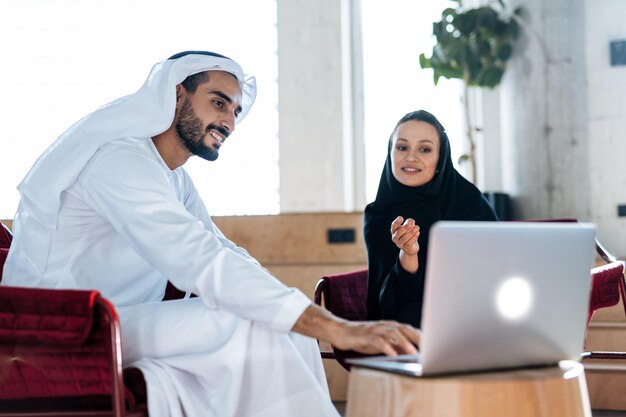 Mann und Frau mit traditioneller Kleidung der Emirate, die in einem Geschäftsbüro von Dubai arbeiten