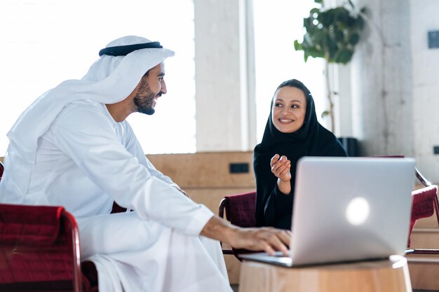 Mann und Frau mit traditioneller Kleidung, die in einem Geschäftsbüro von Dubai arbeiten