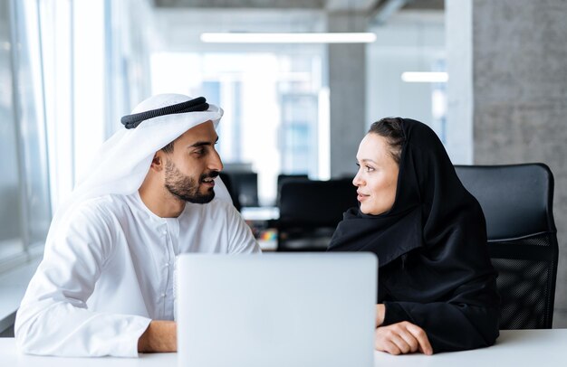 Mann und Frau mit traditioneller Kleidung, die in einem Geschäftsbüro von Dubai arbeiten