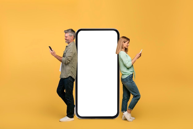 Mann und Frau mittleren Alters, die Smartphones verwenden und sich auf ein großes Telefon mit leerem Bildschirm lehnen, werben Website-Mockup