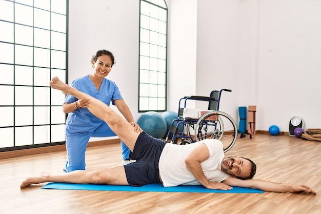 Foto mann und frau mittleren alters, die zuversichtlich lächeln und sich in der physiotherapie-klinik in einer reha-sitzung dehnen