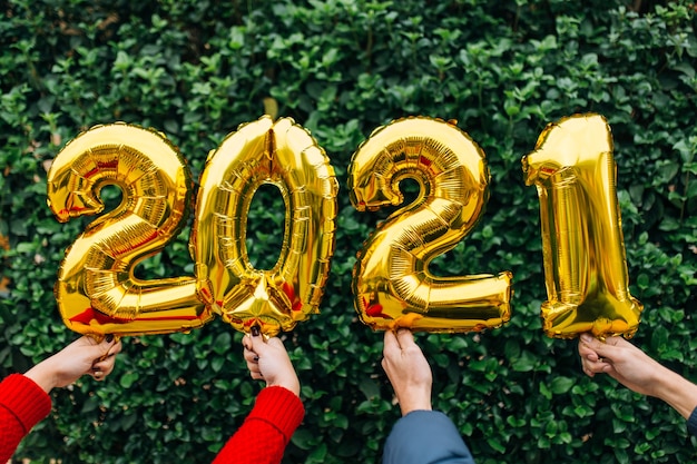 Mann und Frau paar Hände halten Goldfolienballons Nummer 2021 vor einer Wand von Pflanzen. Neujahrsfeierkonzept.