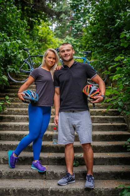 Foto mann und frau posieren im naturpark und halten fahrradhelme.