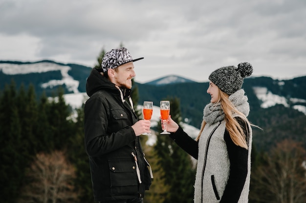 Mann und Frau rösten mit Gläsern Champagner am Winternachtpicknick auf dem Berg. Romantische Liebesgeschichte auf einem Sonnenuntergang. Junges Mädchen und Junge. Vorschlagsideen. Weihnachtsfeier Zeit.